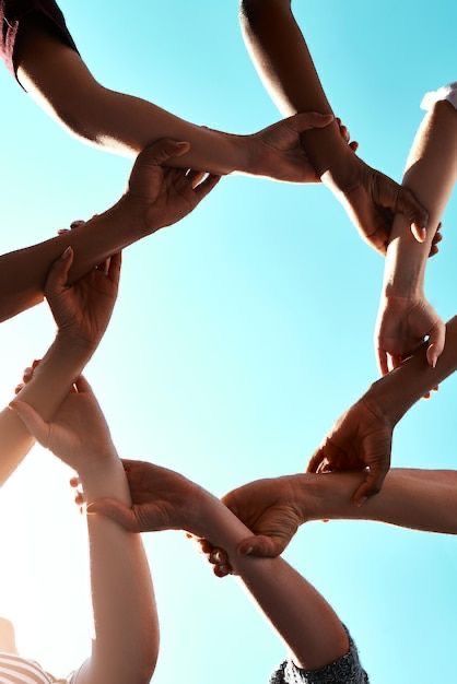 Diverse hands joining together in a circle against a blue sky, symbolizing unity and teamwork